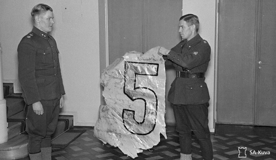 Kuvassa vänrikki Sven-Erik Fagerholm ojentaa luutnantti Sarvannolle peräsimen kappaleen yhdestä hänen alasampumastaan pommikoneesta 8. tammikuuta 1940. (Kuva: SA-kuva) 