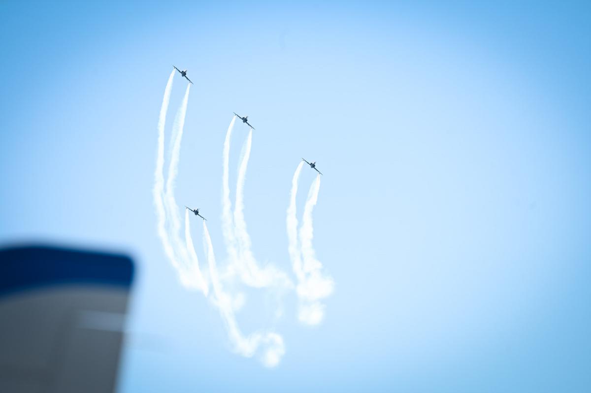 Kolme Hawk-suihkuharjoituskonetta lentää rivissä alapuolellaan neljäs kone. Koneet jättävät jälkeensä valkean vanan siniselle taivaalle.