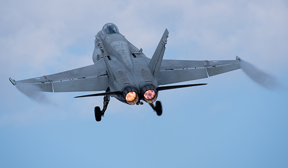 Hornet -hävittäjä takaa kuvattuna nousemasssa pilviselle aivaalle.