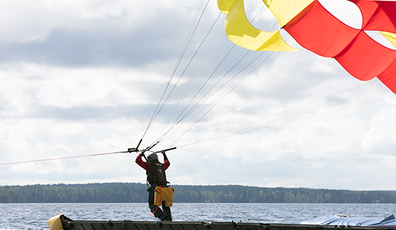 Lentäjä järven rannalla laskuvarjo yläpuolellaan valmistautumassa hinausvarjoharjoitukseen