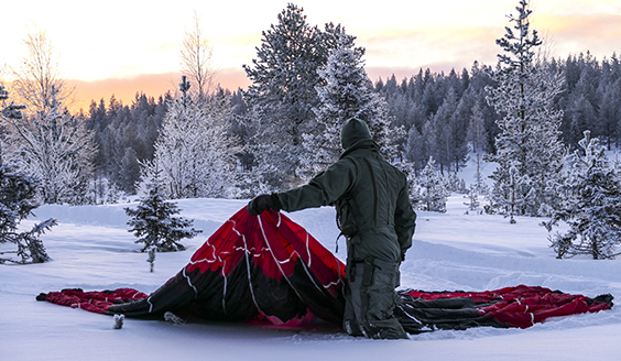 Lentäjä lumisessa maisemassa punaisen laskuvarjon kanssa