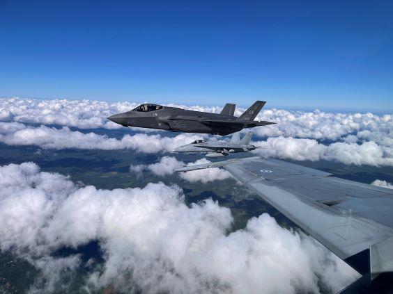 A US F-35 fighter with Finnish Hornet fighters flying above clouds in summer