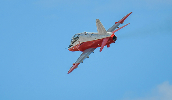Punavalkoinen Hawk-suihkuharjoituskone ilmassa sinistä taivasta vasten