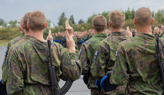 Nuorten miesten joukko sotilaspuvussa antamassa sotilasvalaa, kuvattuna takaapäin.