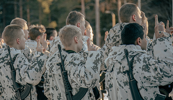 Varusmiesryhmä vannomassa sotilasvalaa selkäpuolelta kuvattuna aurinkoisena päivänä.