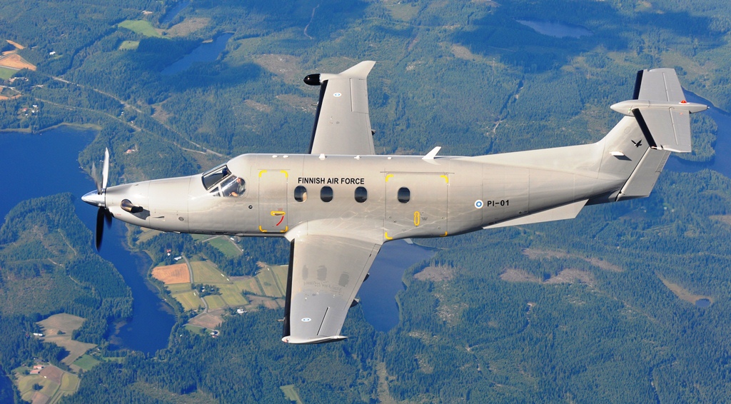 Ilmavoimien Pilatus PC-12 NG -yhteyskone lentää taivalla. Kone on kuvattu ylhäältä käsin ja taustalla näkyy maata sekä vesistöjä.
