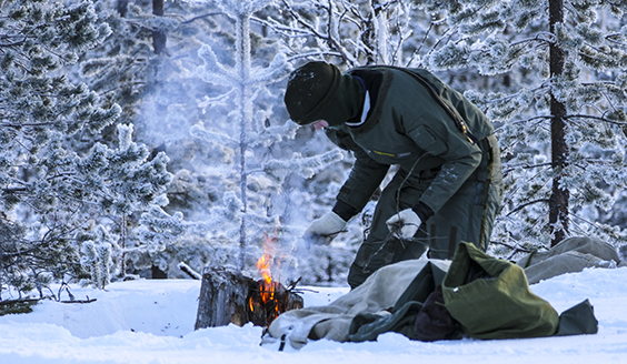 Yksi henkilö sytyttää tulta lumisessa metsämaisemassa