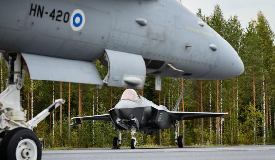 Suomalaisessa maantietukikohdassa otettu kuva, jossa etualalla näkyy suomalaisen Hornet-hävittäjän keulaa ja taaempana norjalainen F-35-hävittäjä. Taustalla suomalaista, syksyistä sekametsää.