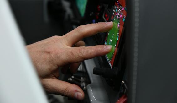 Lähikuva Grob-alkeiskoulukoneen ohjaamosta, jossa lentäjä käsittelee sormillaan yhtä ohjaamon kosketusnäyttöä.