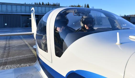 Lähikuva Grob-alkeiskoulukoneesta, jossa kaksi henkilöä valmistautuu lähtemään lentokoneella liikkeelle.