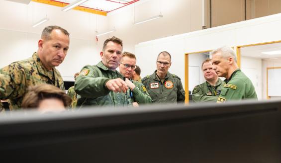 Kuusi sotilasasuun pukeutunutta miestä keskustelee tarkastellessaan tietokonetta, jonka tumma selkämys täyttää kuvan etualan.