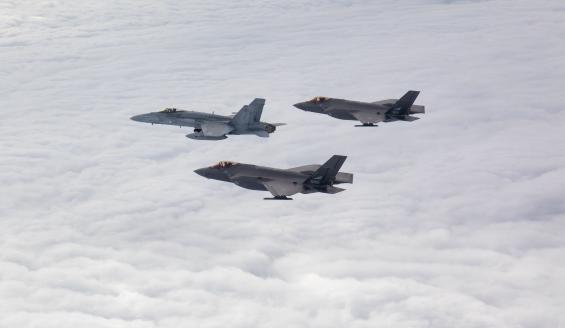 Ilmassa otetussa kuvassa kaksi norjalaista F-35-hävittäjää lentää suomalaisen Hornet-hävittäjän siivellä valkean pilvipeitteen yllä. 