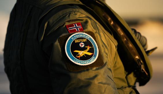 Lähikuva lentäjän olkavarresta, jossa hihamerkkeinä Norjan lippu sekä norjalainen lentokoulutusmerkki.