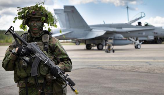 Varusmies seisoo taisteluvarustuksessa, Hornet-monitoimihävittäjä taustalla.