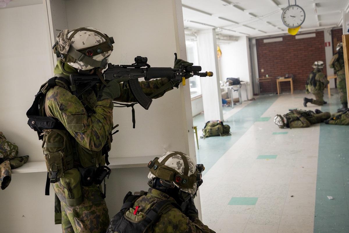 Aseistetut maastopuhkuiset varusmiehet harjoittelevat koulurakennuksen sisällä.