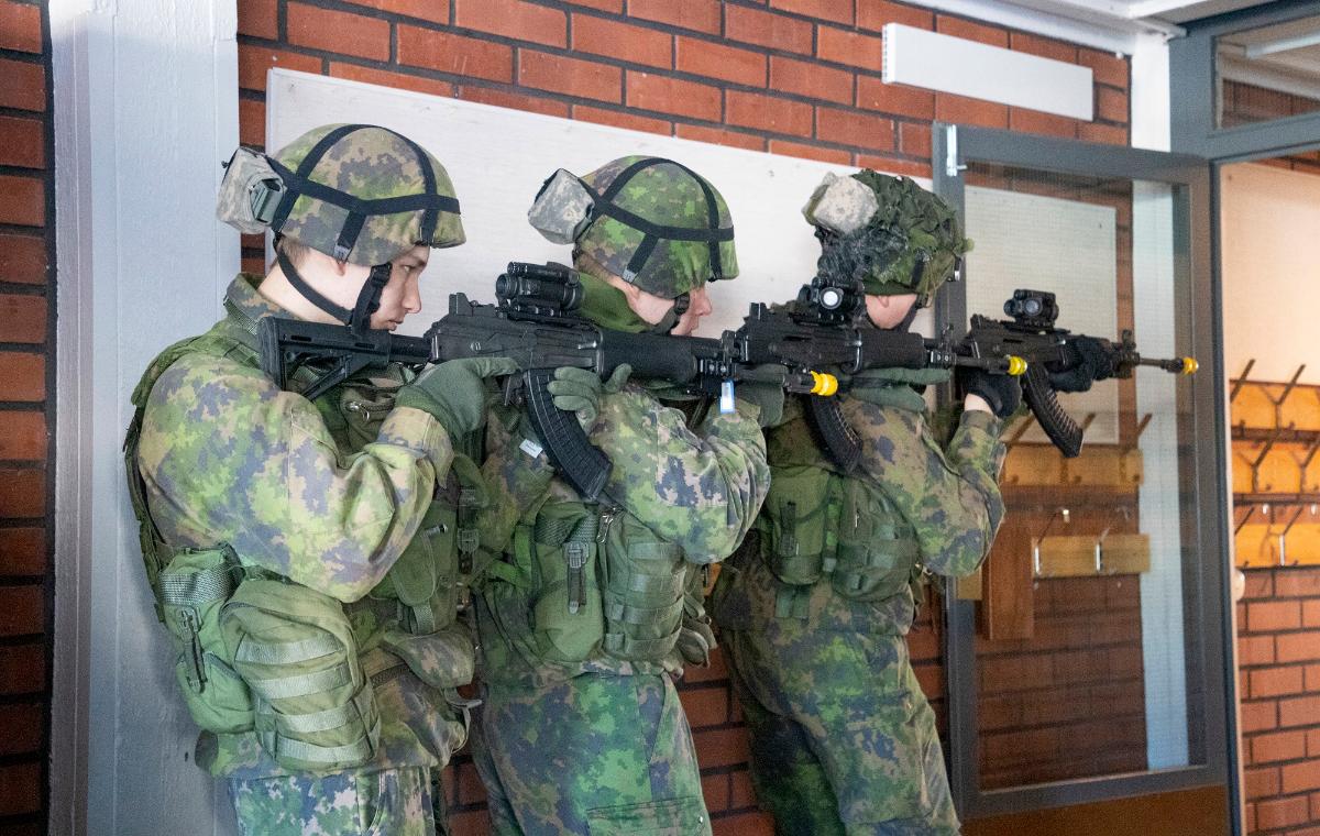 Kolme varusmiestä maastopuvuissa ja rynnäkkökiväärien kanssa harjoittelemassa rakennuksen sisätiloissa.