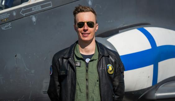Henkilökuva hymyilevästä lentäjästä aurinkolasit silmillään Hawk-suihkuharjoituskoneen edessä. 