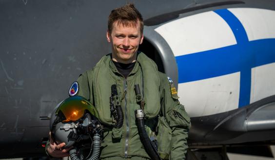 Henkilökuva hymyilevästä lentäjästä varusteissaan Hawk-suihkuharjoituskoneen edessä. 
