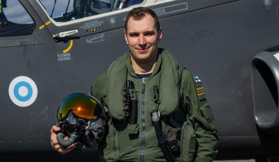 Henkilökuva hymyilevästä lentäjästä varusteissaan Hawk-suihkuharjoituskoneen edessä. 
