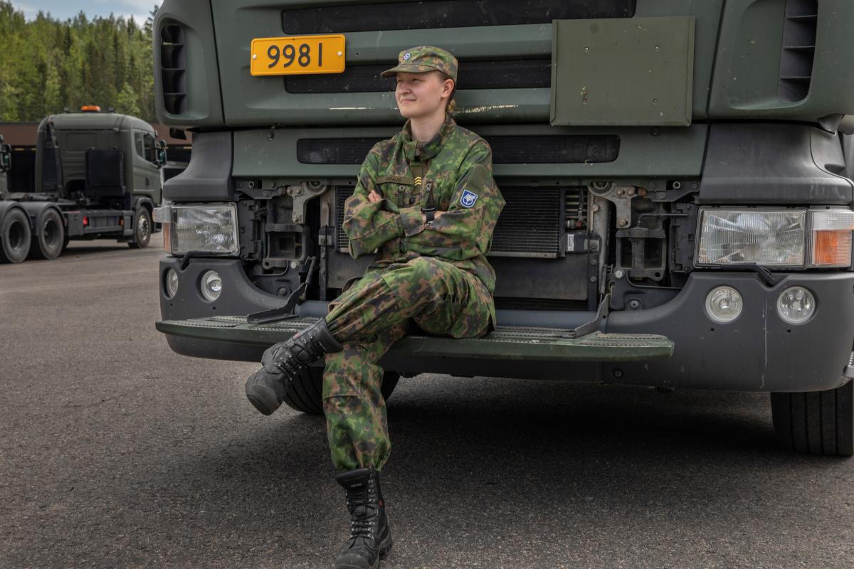 Kersantti Veera Emaus istuu puolustusvoimien kuorma-auton etupuskurilla alahelman päällä.