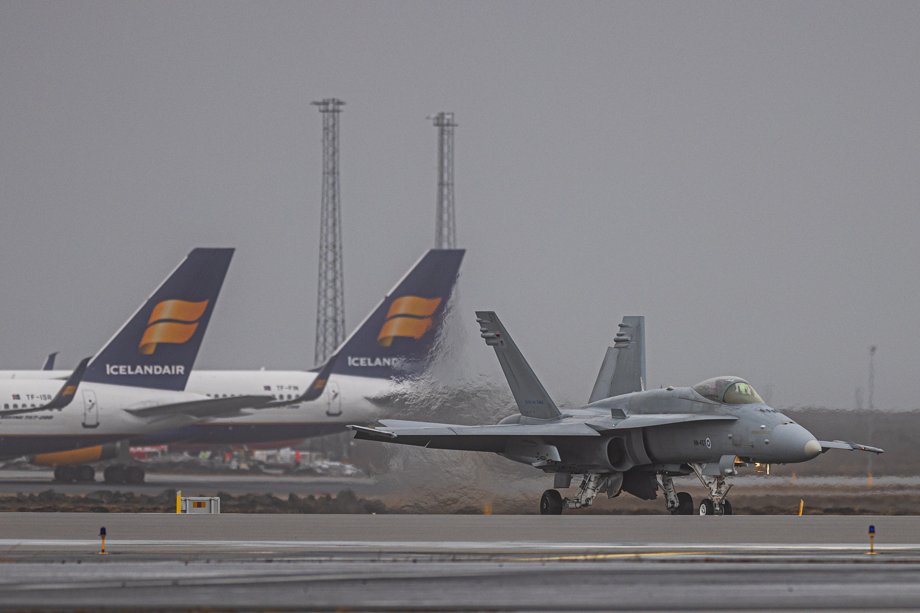 Hornet rullaa lentokenttäalueella taustallaan Icelandair-lentoyhtiön matkustajakoneita. 