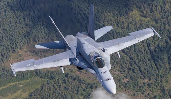 F/A-18 Hornet monitoimihävittäjä lentää ja taustalla näkyy maata.